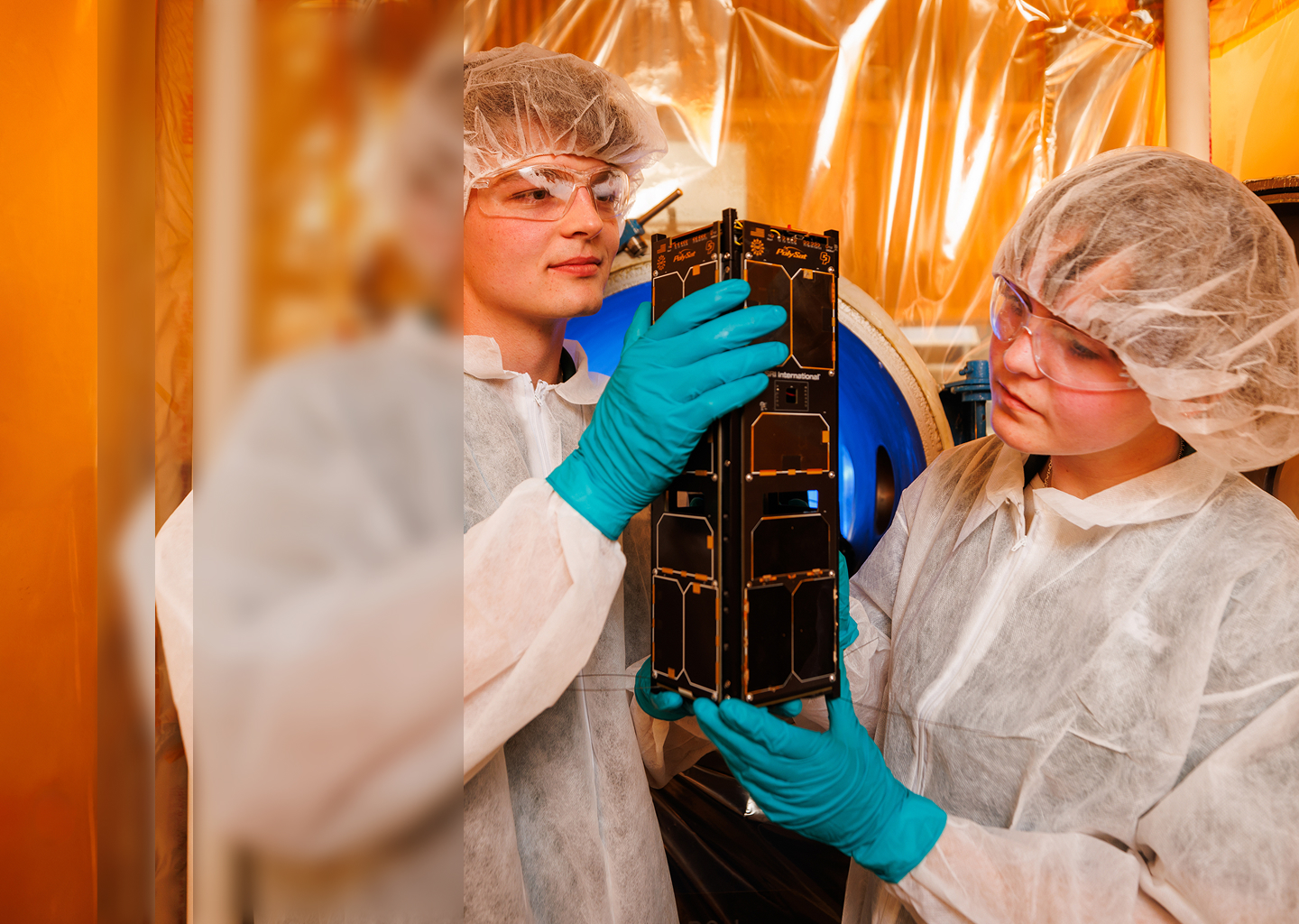 Two students in a clean room examining a satellite