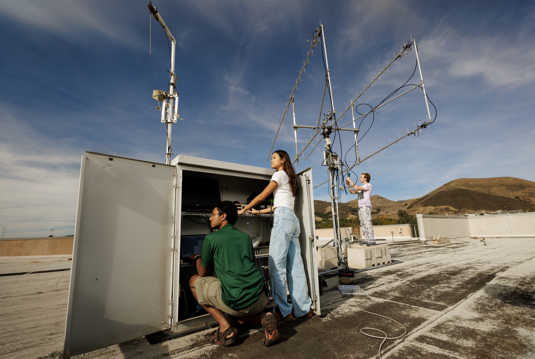 Three students working on antennae on a rooftop